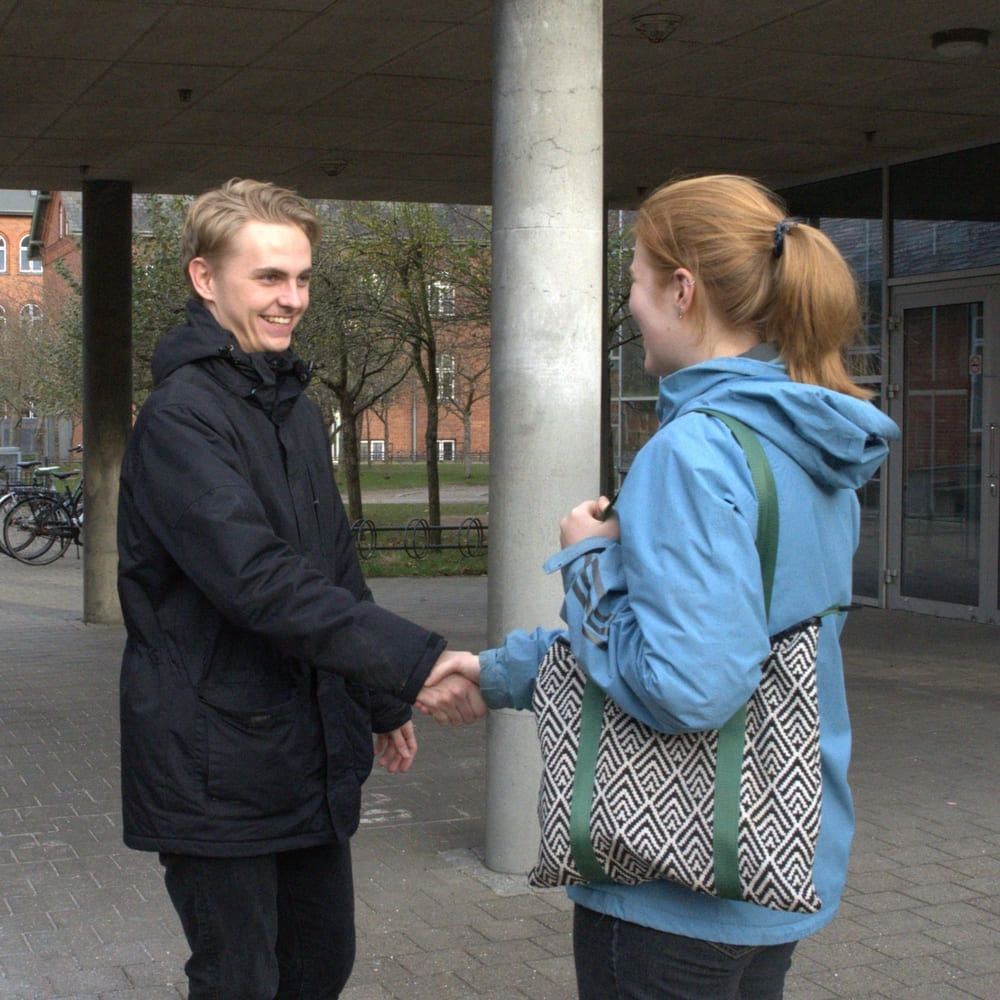 Uden for en indgang står en buddy og byder velkommen samt giver hånd til et potentielt nyt medlem.